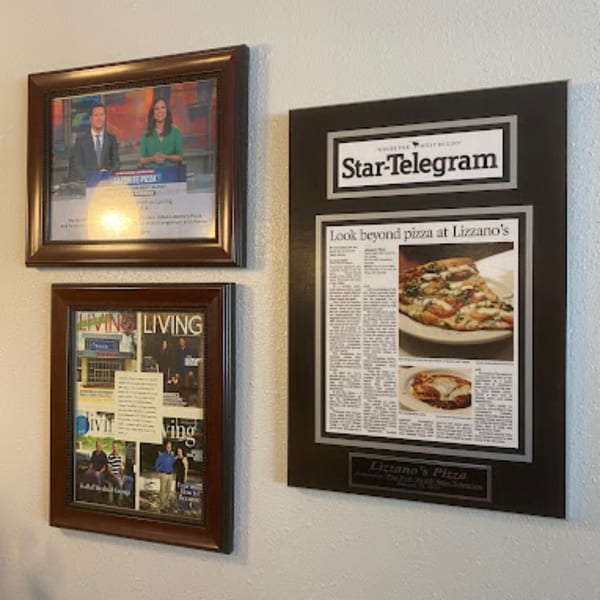 Framed newspaper and magazine articles about Lizzano's Pizza, featuring food and people, hanging on a white wall.