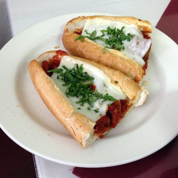 Two Lizzano's Pizza meatball subs with melted mozzarella cheese and fresh basil on a white plate.