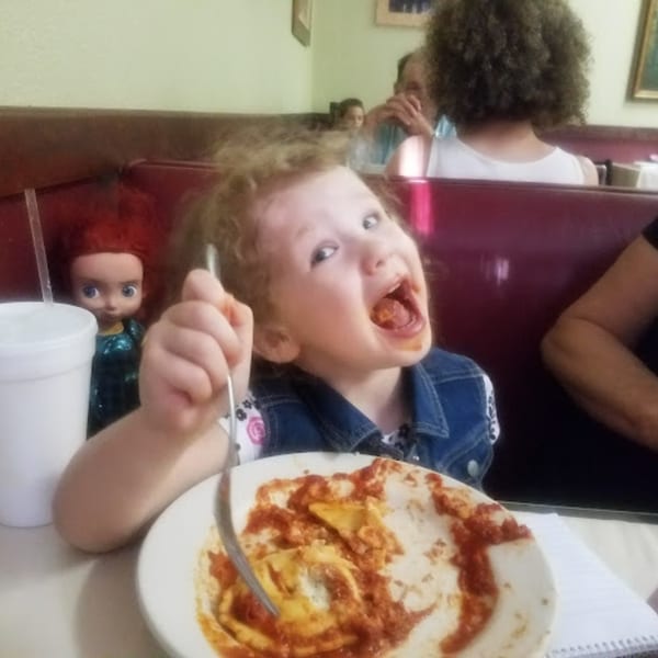 A young child with a messy face happily eats ravioli with red sauce at Lizzano's Pizza.