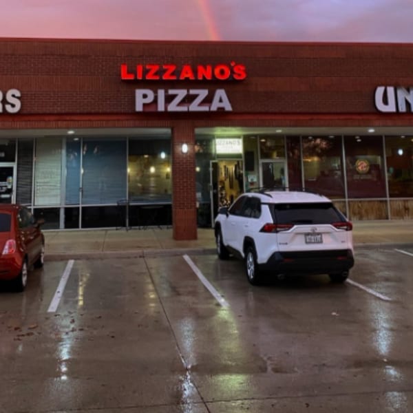Exterior of Lizzano's Pizza, a brick building with red and white signs, and cars parked in front.