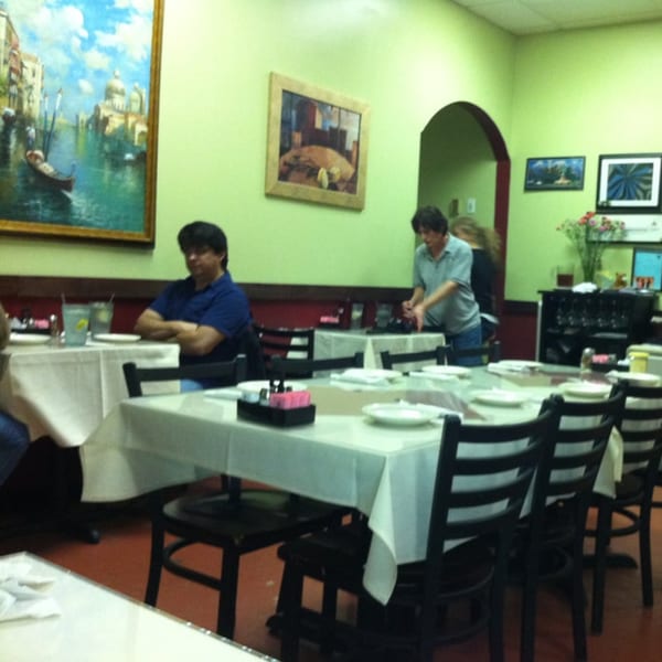 Lizzano's Pizza dining room with patrons, white tablecloths, and Italian-themed artwork on light green walls.