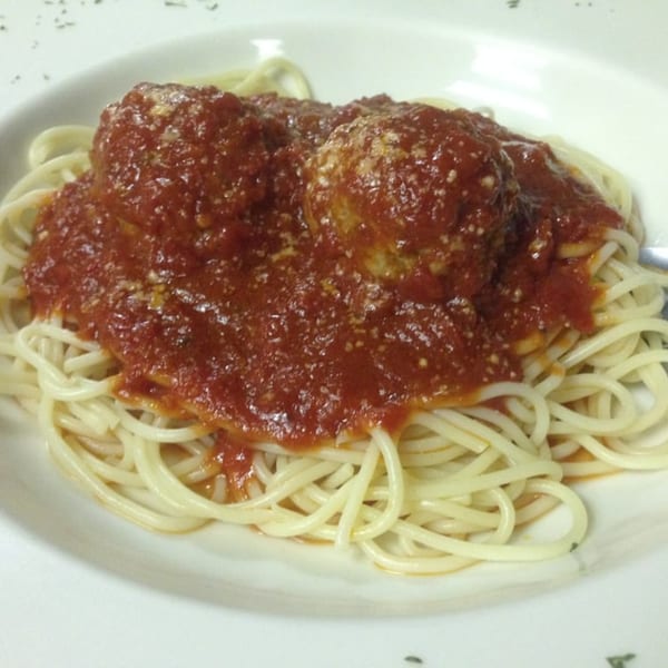 Spaghetti with two large meatballs covered in red sauce and sprinkled with cheese on a white plate.