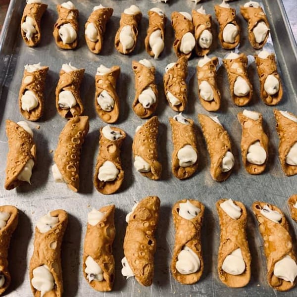 Rows of freshly made Lizzano's cannolis with creamy white filling on a metal baking sheet.