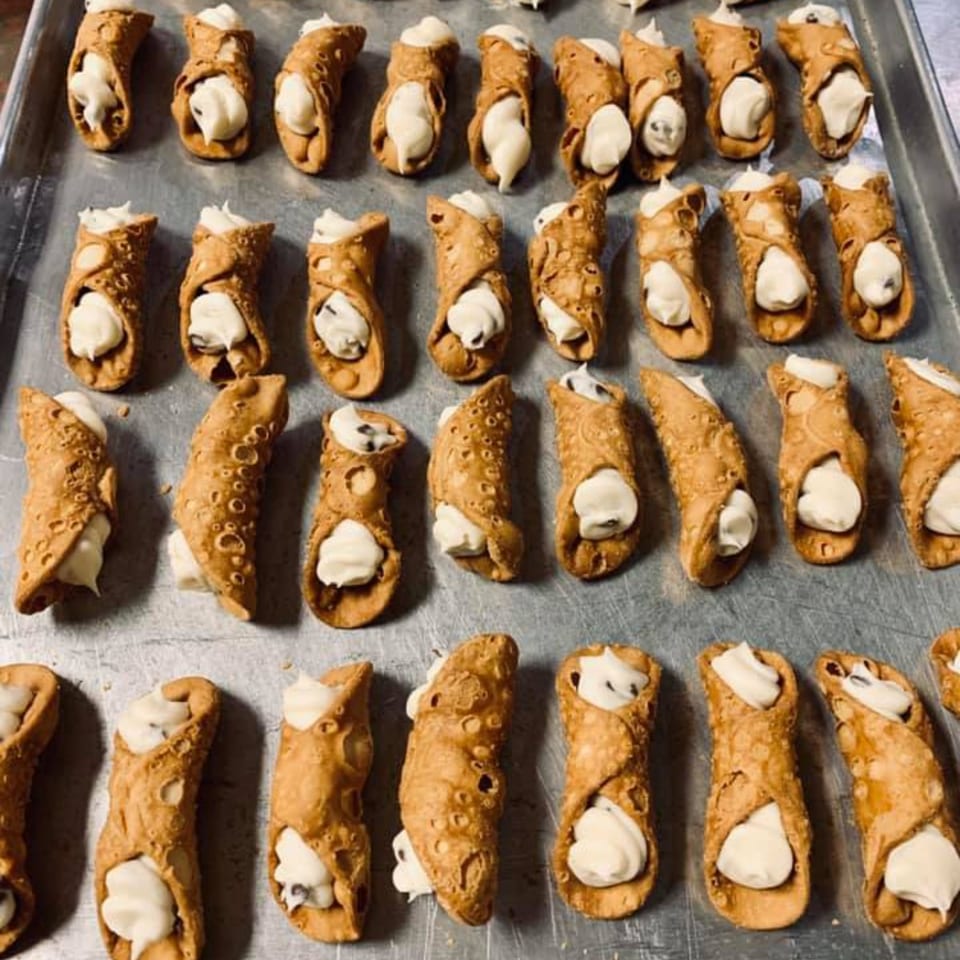 Rows of freshly made Lizzano's cannolis with creamy white filling on a metal baking sheet.