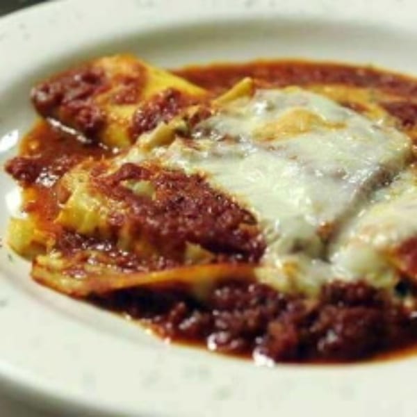 Baked ravioli with rich red sauce and melted mozzarella cheese on a white plate.