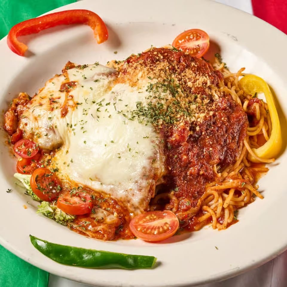 Chicken parmesan with melted mozzarella, marinara, spaghetti, and cherry tomatoes on a white plate.