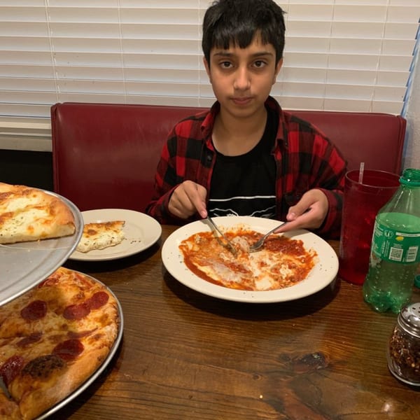 A young boy eating pasta at Lizzano's Pizza, with a pepperoni pizza and a white pizza nearby.