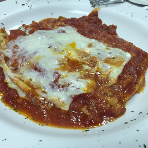 Lizzano's Pizza lasagna, topped with melted mozzarella cheese and rich red sauce, on a white plate.