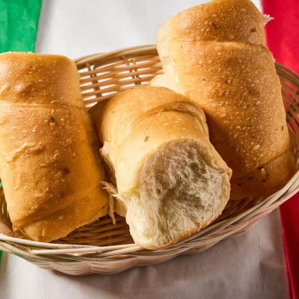 A wicker basket filled with several golden-brown Italian breadsticks, against a red, white, and green background.