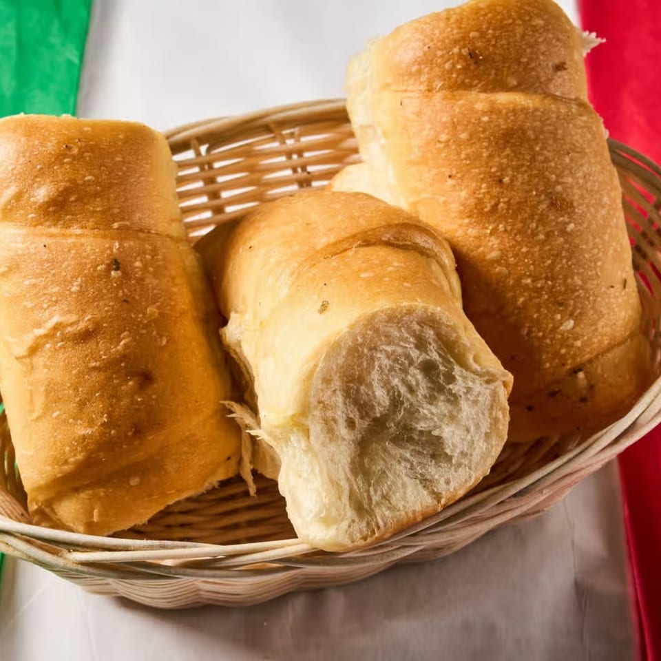 A wicker basket filled with several golden-brown Italian breadsticks, against a red, white, and green background.